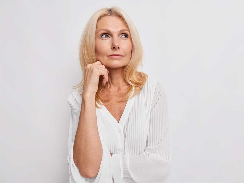 mulher pensativa com uma mão apoiada sobre o queixo